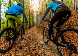 Mountain biking in autumn landscape forest. Man and woman cycling MTB flow uphill trail.