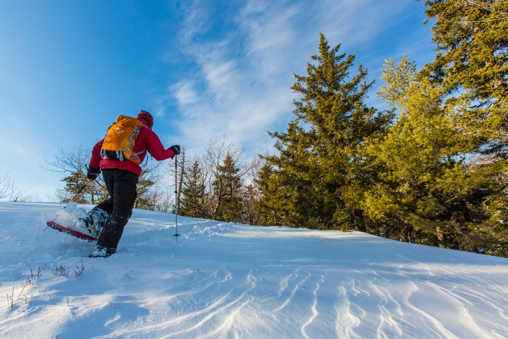 Things to do in New Hampshire, man enjoying the snow with a sled and snowshoeing 