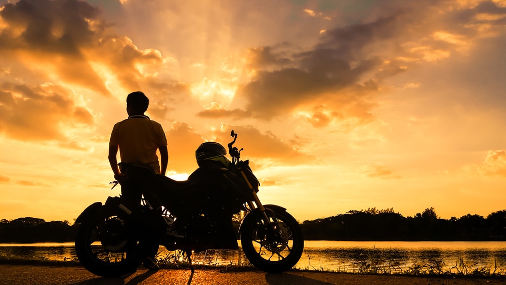 Laconia Bike Week, photo of a man with his motorcycle looking out at the lake 